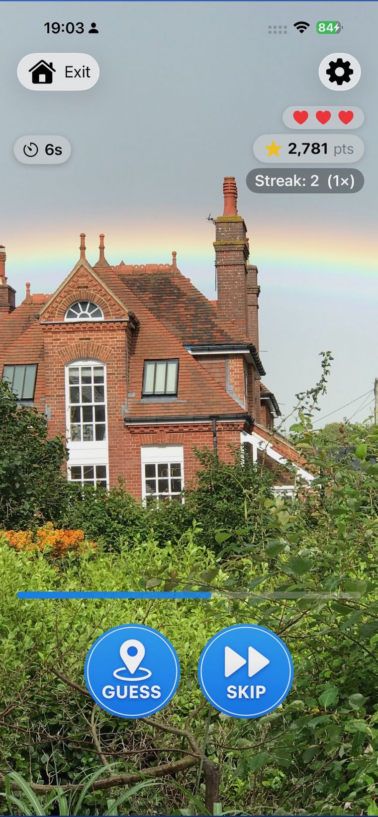 Zoom Quest gameplay — a red-brick house under a rainbow with Guess and Skip buttons